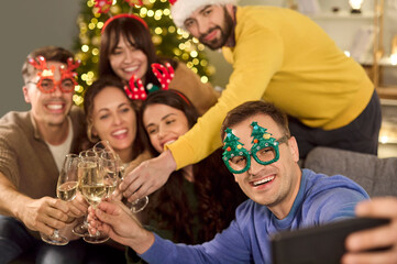 Christmas friends celebration with champagne toast. Gathered at a home party, they laugh, clink flutes, and lean in for a selfie in Santa hats. Joyful holiday selfie and warm celebration.