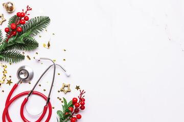 Christmas medical banner with festive sparkling decorations, fir tree branches and medical stethoscope on white marble background with copy space for your design.