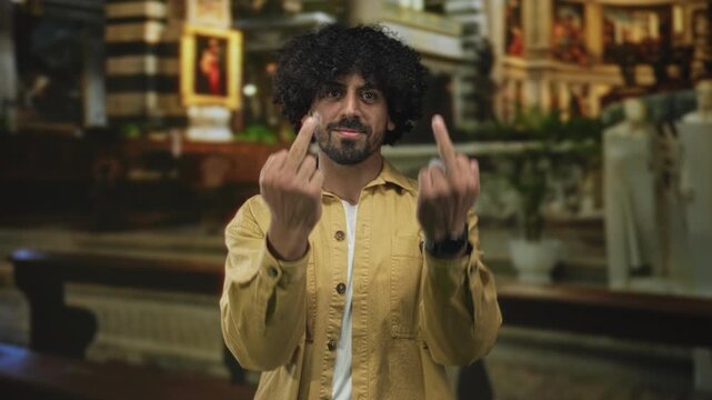 Man with curly hair shows middle fingers with bare hands in church building interior near pews and altar; defiance protest.
