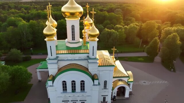 A majestic building features golden domes rising above lush green trees, creating a stunning backdrop as the sun sets on the horizon. The ornate details of the architecture are hig