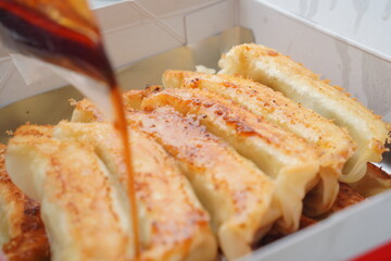 焼き餃子にタレが注がれる動きのある瞬間を捉えた一枚。湯気と油の光沢が食欲を刺激し、レシピ・食レポ・広告・SNS用ビジュアルに最適。動きのあるフードフォトとして印象的な素材