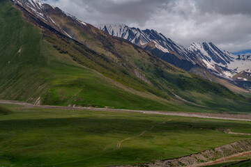 Stormy light over sweeping green slopes and jagged snowy ridge