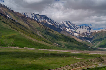 Stormy light over sweeping green slopes and jagged snowy ridge