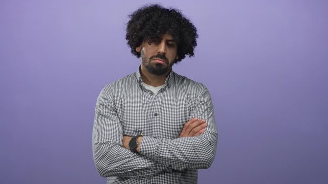 Man with arms crossed and wristwatch visible in studio set against a solid purple wall; pensive reflection.