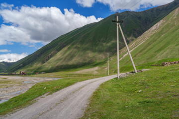 Gravel track and power lines beneath long green Caucasus slopes
