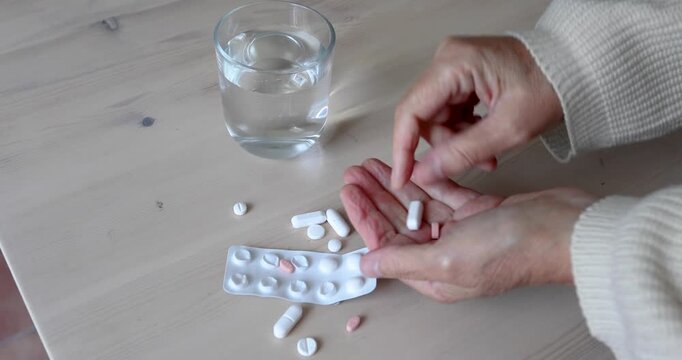 Hands collecting multiple pills and taking a glass of water. Female hands gathering several scattered tablets.  Heavy medication intake or age-related polypharmacy. No audio.