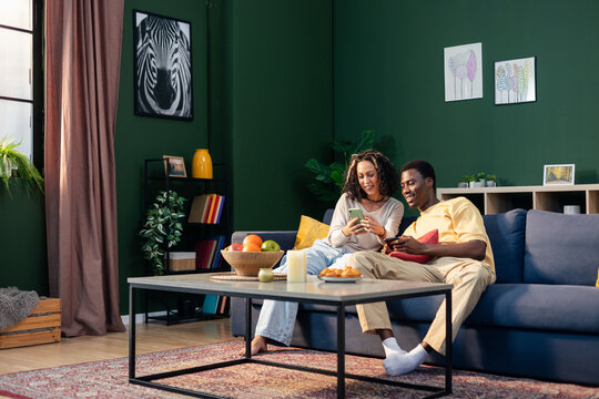 Diverse couple relaxing on couch, enjoying smartphones together