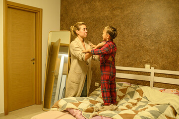Mother and son at home preparing for bedtime, putting on pajamas, reading a book, mother kissing her child and tucking him into bed. Family bonding, love, bedtime routine.