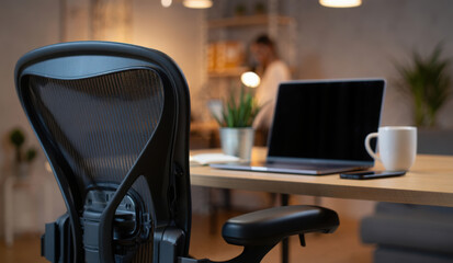Modern remote work concept. A cozy home office with an ergonomic chair in front of a wooden desk with a laptop and a coffee mug