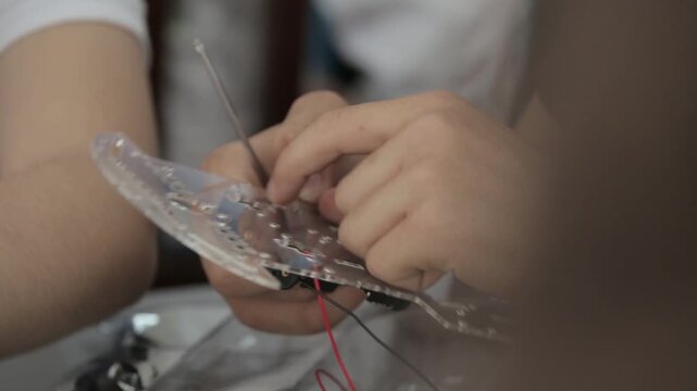Students assemble DIY robot car and test LED circuits on breadboard. STEM education process showing electronics, wiring, programming, and engineering skills in a classroom setting.

