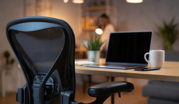 Modern remote work concept. A cozy home office with an ergonomic chair in front of a wooden desk with a laptop and a coffee mug - Powered by Adobe