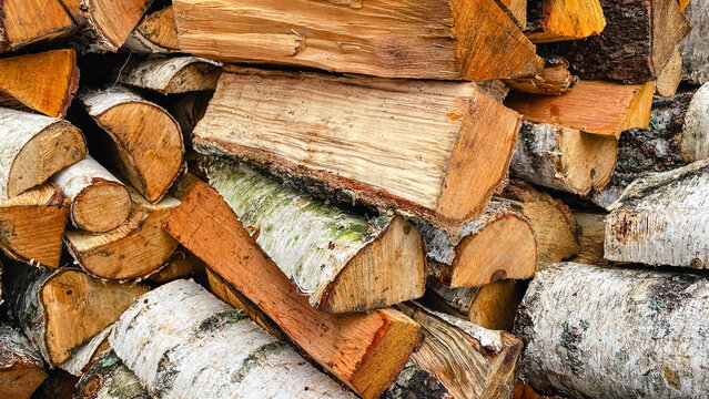Detailed close-up of stacked birch firewood logs, showing white bark and rough textured wood ends