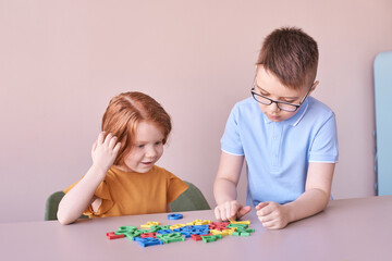 Fototapeta premium Caucasian children playing with colorful alphabet letters at a table.