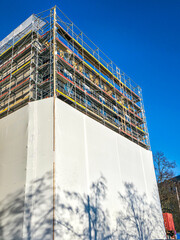 Building under renovation covered with scaffolding and protective sheeting against blue sky