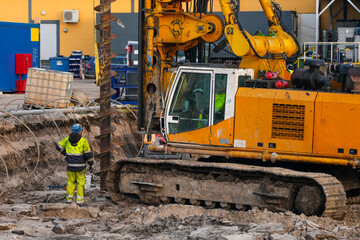 Heavy drilling machine operating at construction site with worker supervising foundation excavation