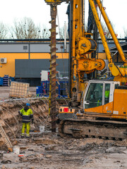 Construction worker supervising large drilling rig during foundation excavation at building site