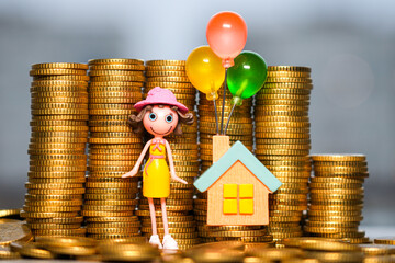 Dream Home Savings Concept with Toy House, Balloons and Figurine Surrounded by Stacked Gold Coins