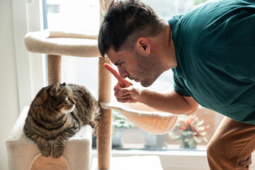 Man scolding tabby cat with pointing finger at home