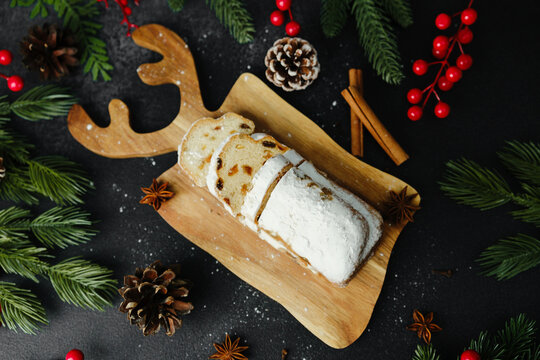 Fruitcake on reindeer shaped board with pine cones cinnamon and festive berries on dark background - Powered by Adobe