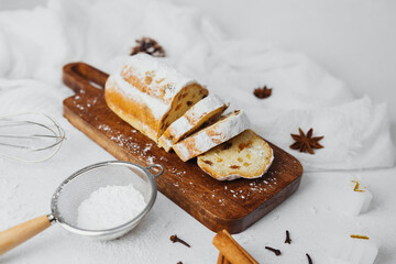 Sweet bread loaf with dried fruit and powdered sugar on wooden board with baking tools