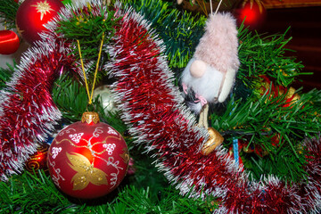 Close-up of a red painted Christmas ornament and a cute gnome figurine with a pink hat hanging on a decorated Christmas tree. Festive holiday decor scene, perfect for Christmas design, greeting cards,