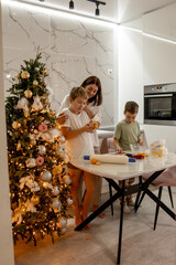 Mom and the kids are getting ready for the New Year by making cookies in the kitchen and having fun together at the Christmas tree.
