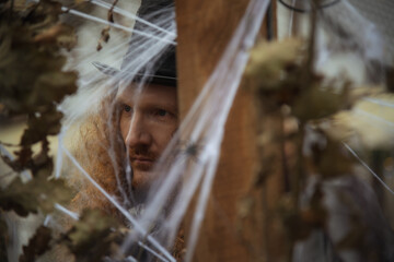 Mysterious figure surrounded by cobwebs in a dimly lit setting