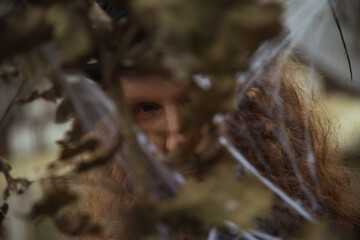 Person hidden behind autumn leaves in a mysterious forest scene