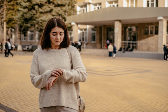 a girl is looking at her watch outside, waiting for someone