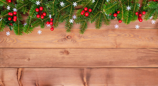 Natural Christmas border with fir branches and red holly berries on wooden background