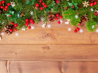 Christmas composition with green fir branches, red berries, pine cones and white snowflakes on wooden background