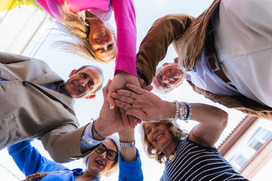 Mature friends stacking hands together symbolizing unity and teamwork