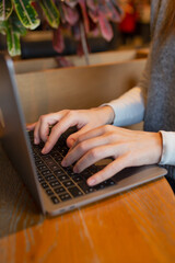 A close-up of a woman's hands typing on a laptop keyboard in a cafe. A businesswoman or student uses a PC for online marketing, freelancing, working from home, online education, and distance learning.