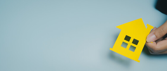 Yellow house cutout hand holding paper house real estate concept home ownership property investment minimal background bright color paper craft small house model isolated object