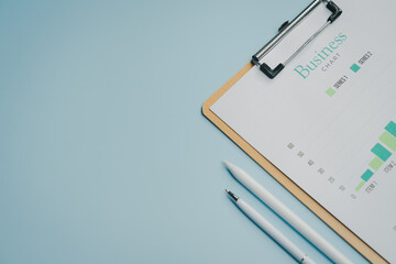 Business chart with bar graph on clipboard and two pens on blue background, minimal workspace concept with copy space for text or design