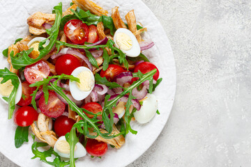a warm salad with fried chicken fillet, arugula and cherry tomatoes, and boiled quail eggs, on a white plate, no people.