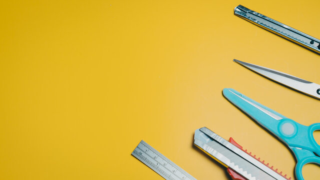 Stationery tools, scissors, cutter knife, metal ruler, and utility knife on yellow background, creative workspace with office supplies for cutting and measuring