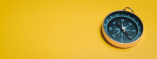 Black compass on yellow background with metal frame and needle pointing north © JK_kyoto