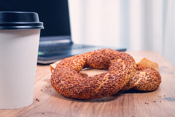 simits with coffee on a wooden table, with a laptop, in a cozy working environment, snack, breakfast, no people,