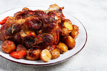 Pork knuckle baked with vegetables, new potatoes , on a white plate, homemade, no people,