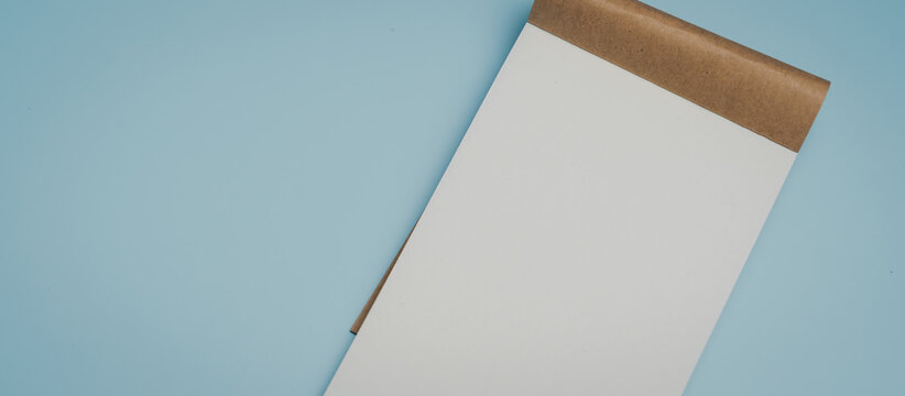 Blank notepad on blue background with brown cover, minimalistic stationery for notes or sketches, clean and simple design inspiring creativity and organization