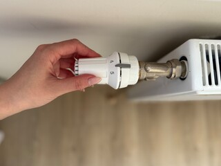 hand holding a radiator. White heating battery regulator with the possibility of mechanical adjustment of the intensity of room heating.