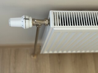 White steel radiator on the background of a beige wall.
The heating level is regulated by a handle.