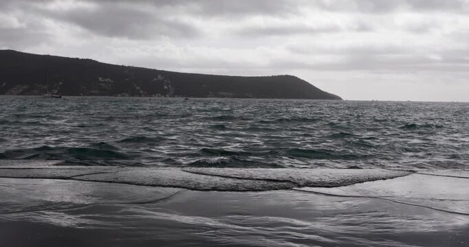 Empty beach at seaside at early autumn, Boka bay, Adriatic sea, Montenegro, Mediterranean, waves flushing concrete beach on cloudy day