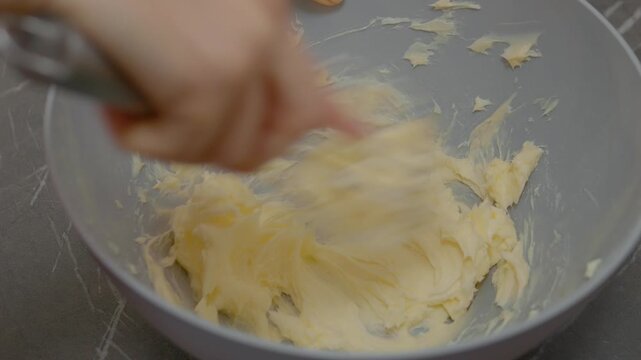 A woman combines soft butter in a large bowl, preparing for her baking project in a warm and inviting kitchen, showcasing careful mixing techniques.
