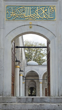 View of an arched gateway adorned with intricate gold Arabic script, leading to a serene courtyard with white stone columns, Istanbul, Istanbul, Turkey.