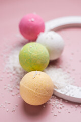 Bath bombs with scattered sea salt on a pink background. At-home spa treatments for relaxation and restoration. Fizzing bath bombs for aromatherapy and skin care. Cosmetic product
