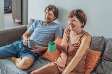 Older woman and her adult son relaxing together on the sofa while watching a comedy on television, enjoying a warm family moment at home. Entertainment, bonding and cozy lifestyle concept