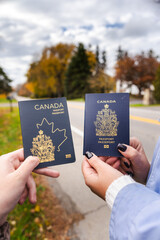 Two people outdoors holding Canadian passports side by side, showing the covers clearly against an...