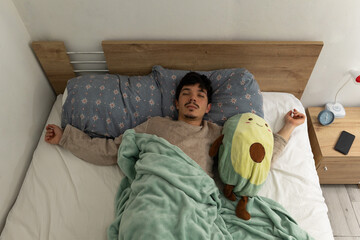 Top view of a man lying in his bed, sleeping deeply while wearing his pajamas. A calm scene ideal for concepts of rest and restorative sleep
